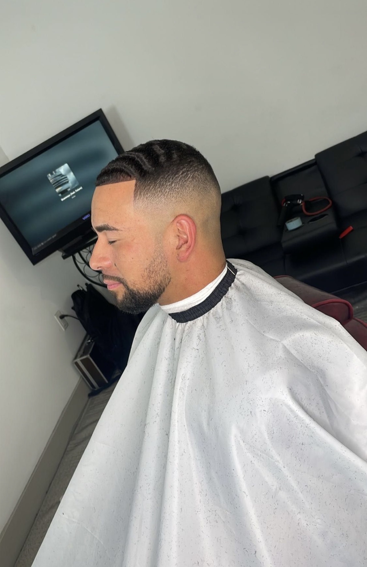 Man with a clean fade haircut, waves and a lineup wearing a white barber cape